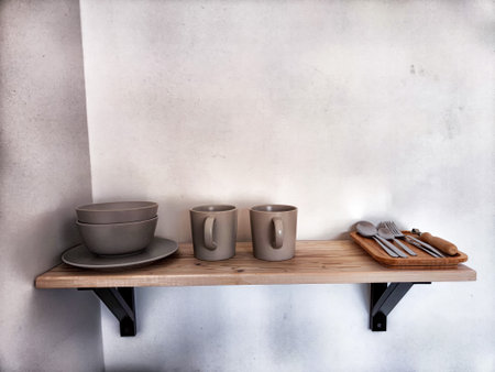 Two ceramic mugs and stacked ceramic bowls sit on wooden shelf in a kitchenの写真素材