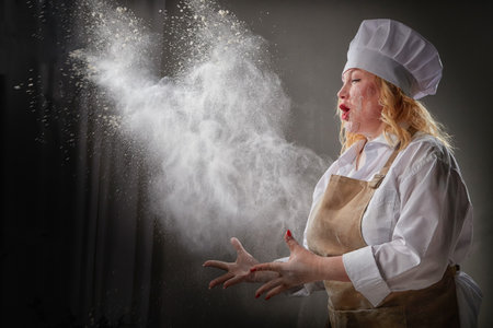 A fat funny female cook in a hat and apron posing and taking selfie in the kitchen with flour. Cooking, body positive, cloud, smoke, flourの写真素材