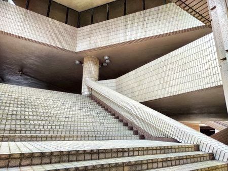 A low-angle view of a modern building's entrance, featuring tiled stairway leading up to a large overhang with exposed ceiling lightsの写真素材