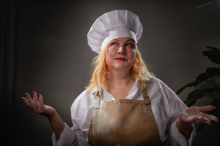A funny female cook in a hat and apron poses in the kitchen and takes a selfie. Good cookingの写真素材