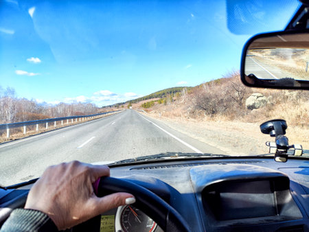 Car salon, windshield, hand of woman on steering wheel and landscape. View from seat of driver on nature landscape. Single trip of female travelerの写真素材