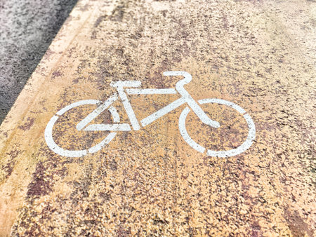 A clear, bright white bicycle symbol has been painted onto a textured pavement surface to enhance...