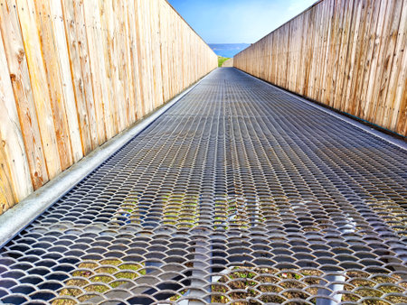 Metal grating walkway between two wooden fences, with green grass visible below. background, texture, pattern, frame, place for text, copy spaceの写真素材
