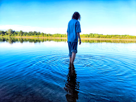A tourist girl steps into the chilly water of a river, enjoying the refreshing experience on a...