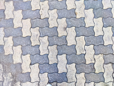 Pavement features interlocking tiles in a wavy pattern under bright daylight.