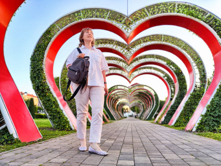 A middle-aged woman strolls through vibrant floral arches at a park during a sunny dayの写真素材