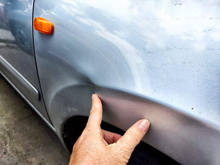 A person is now pointing at a severely damaged car fender, highlighting the extent of the damage that has occurred on the vehicleの写真素材