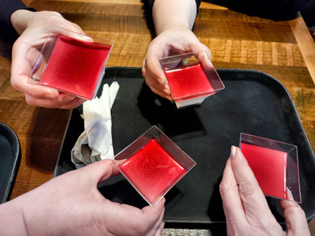 Four hands lift square jelly desserts in vibrant red while gathered around a wooden table at a...