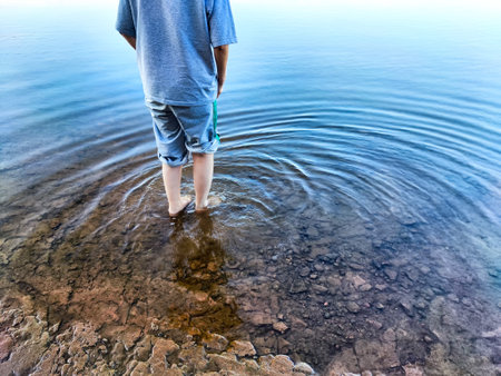 A tourist girl steps into the chilly water of a river, enjoying the refreshing experience on a bright, beautiful dayの写真素材