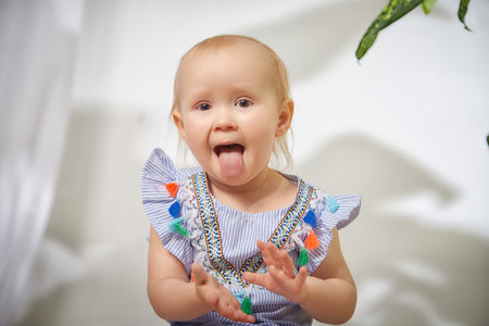 A smiling girl in a blue striped dress sits with arms outstretched on a tan surfaceの写真素材