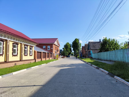 A peaceful street lined with quaint wooden houses, shaded by trees under a clear blue sky.の写真素材