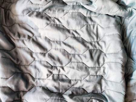 A soft blue quilted blanket lies gently on a bed, illuminated by warm afternoon light in a comfortable living room.の写真素材