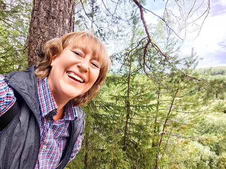 A woman captures a selfie with a breathtaking forest view, sharing her excitement as she explores the beautiful landscapeの写真素材