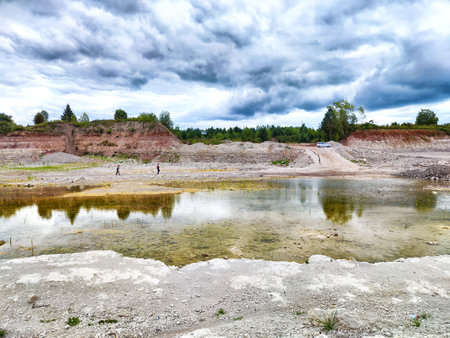 Two individuals stroll alongside calm water reflecting the overcast sky at a quarry.の写真素材
