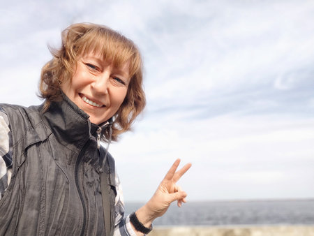 A middle-aged woman smiles broadly while traveling outdoors with a clear sky above her. The adventures of a middle-aged female tourist on tripの写真素材