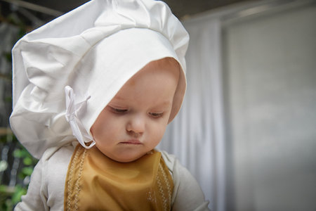 Young girl in a chefs hat poses thoughtfully in a cozy studio setting during a playful photo shootの写真素材