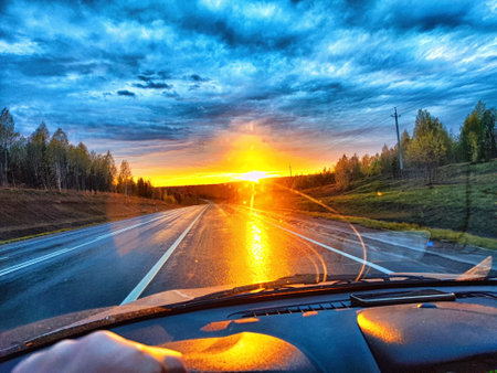 view through car windshield of natural landscape with clouds and sun in sunset. Hand of woman on...