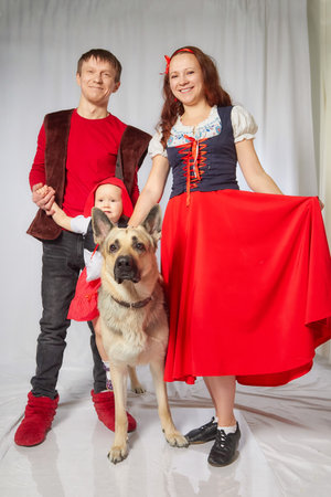 Family in style of fairy tale Little Red Riding Hood and big shepherd dog. Father, mother, daughter in costumes Little red cap and pet as wolfの写真素材