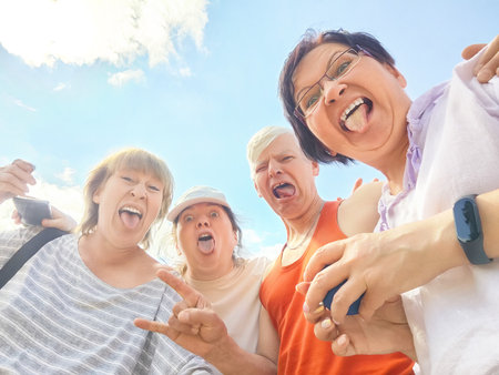 Four friends are happily posing together outdoors, enjoying their time under a bright blue sky on a sunny dayの写真素材