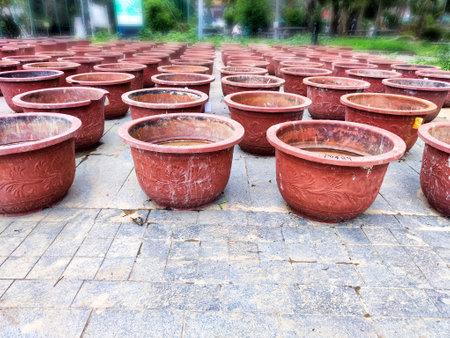 A large collection of red terracotta plant pots sits on a stone surface, surrounded by greenery under bright daylight.の写真素材