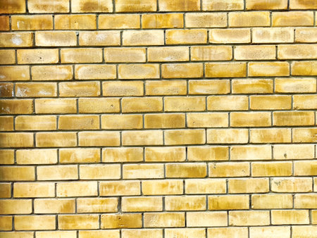 A textured yellow brick wall features a uniform pattern, creating an ideal backdrop for adding text or graphic designs with ample copy space.の写真素材