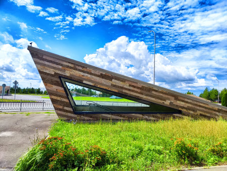 A striking, angled building design stands against a bright blue sky, surrounded by lush greenery and...