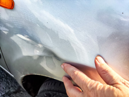 A hand points to a dent on silver car doorの写真素材