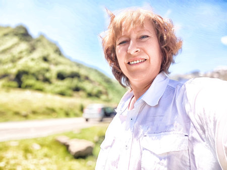 A woman wearing a crisp white shirt is joyfully smiling in front of an impressive mountain backdrop, radiating happiness and warmthの写真素材