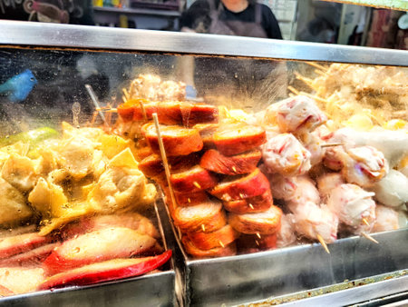Skewers of various meats and seafood are arranged for sale at a busy street food stall.の写真素材