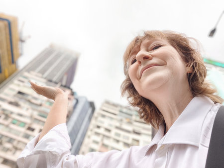 A middle-aged woman who is a tourist and blogger takes selfies near skyscrapers in Hong Kong on a tripの写真素材