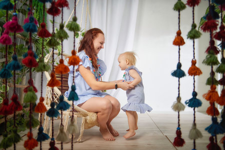 Mother and daughter are playing in the room. Toddler girl is jumping inside. Family recreation and entertainmentの写真素材