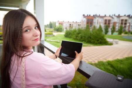 A woman smiles as she looks at her tablet, sitting on a porch with a grassy view and houses in the backgroundの写真素材
