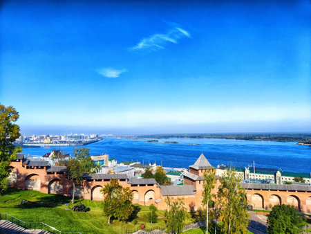 A panoramic view of a river with trees and buildings under a bright blue sky.の写真素材