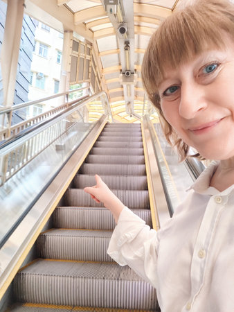 A woman enjoys her journey on an escalator in a vibrant Hong Kong setting. The adventures of middle-aged female tourist on a tripの写真素材