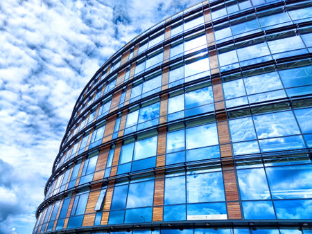 A striking modern features structure a curved glass design mirroring fluffy clouds against a bright...