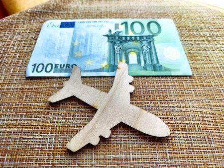 A wooden airplane model rests beside a 100 euro banknote, illustrating the expenses associated with air travel.の写真素材