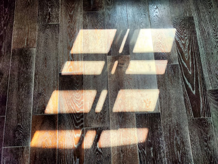 Bright sunlight filters through a window, leaving intricate rectangular patterns on the polished wooden floor.の写真素材
