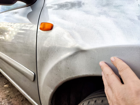 A hand gently touches a noticeable dent on the silver car's side, revealing potential damage in a residential environment.の写真素材