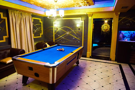 A blue pool table with a few balls on it is set up in game room decorated with gold and blue accents