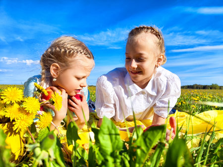 Two girls enjoying a sunny day outdoors in a field of dandelions while sharing apples and laughterの写真素材