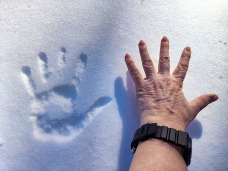 A human hand rests next to a snow imprint, highlighting winter's beauty and unique patterns in fresh snow.の写真素材