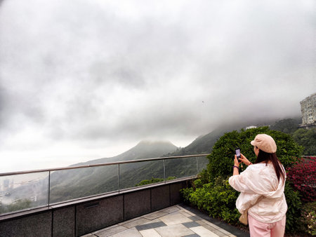 A woman stands on platform capturing the breathtaking view of misty mountains in Hong Kong