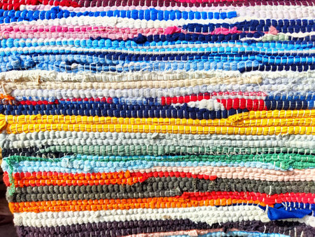 Vibrant strips of fabric stacked in rows display intricate patterns and textures at a busy textile market under bright sunlight.の写真素材