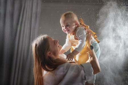 Mother and daughter in aprons joyfully playing with flour during a fun kitchen-themed photo shoot at homeの写真素材