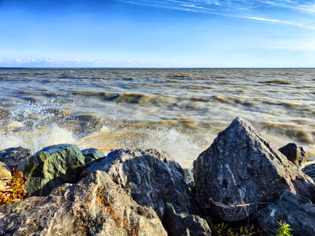 Waves roll onto the rocky shore with a clear blue sky overhead at the lakeの写真素材