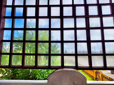 A detailed view of a wooden lattice window reveals lush greenery and a sunny blue sky outside on a peaceful day.の写真素材
