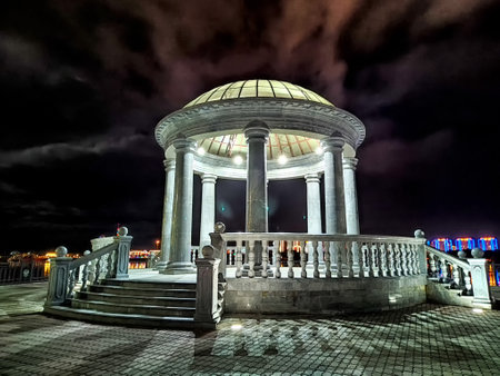 A white stone gazebo with a dome roof and a railing stands under dark sky with cloudsの写真素材