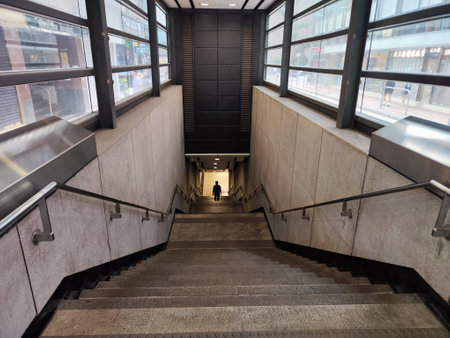 A solitary figure descends the stairs towards underground passage in a bustling cityの写真素材