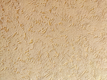 A textured beige wall surface displays a unique pattern with subtle variations in light and shadow, ideal for backgrounds.の写真素材