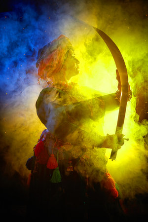 A woman in a colorful headscarf and jewelry poses with a saber in front of a wall of colorful tassels and smoke aroundの写真素材
